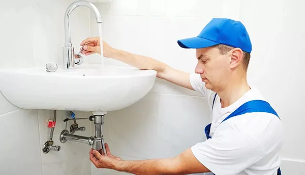 Professional plumber detecting and repairing leak under bathroom sink during leak detection service in Garland TX.