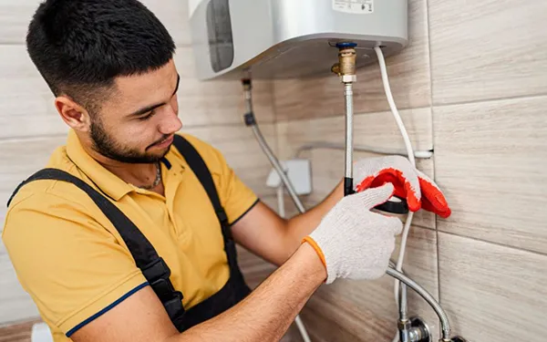 Young plumber using power tool to repair pipe under bathroom sink during residential plumbing installation in Forney TX.