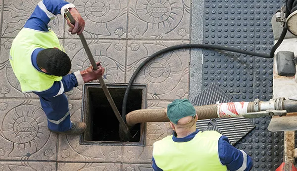 Two workers operating sewer drain cleaning machine and hose inserted into outdoor drain pipe in Garland TX.