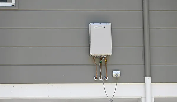 Tankless water heater mounted on exterior gray house wall with benefits of tankless water heater services listed.