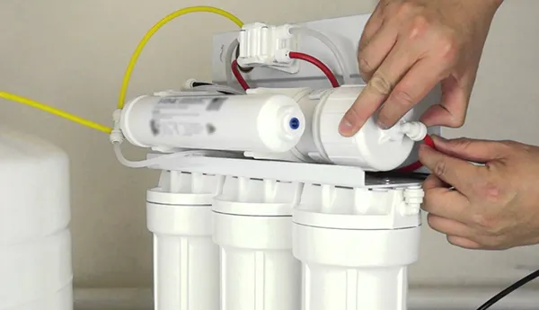 Close-up of technician hands assembling or maintaining a multi-stage water filtration system indoors.