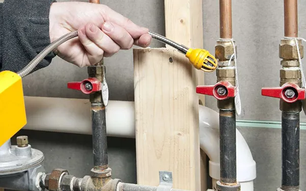 Hand adjusting a yellow valve on metal gas pipes in a utility area.