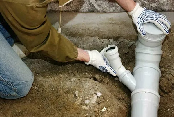 Technician kneeling and working on connecting PVC sewer pipes in a trench.