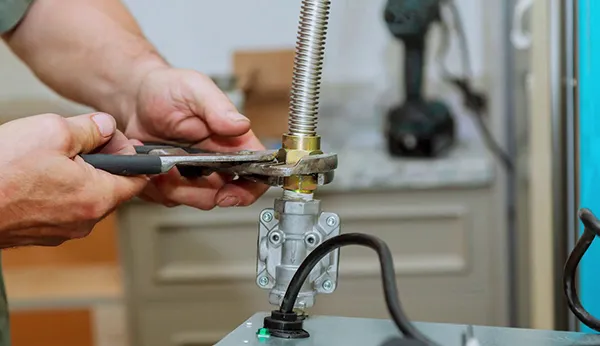 Close-up of plumber’s gloved hands working on a gas pipe fitting with a wrench.