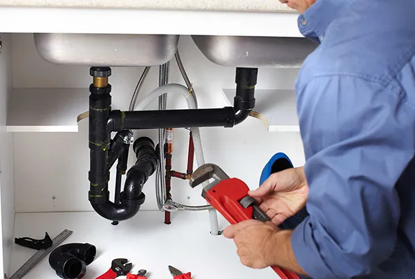 Plumber using wrench to fix leaking pipe under kitchen sink during emergency plumbing repair in Heartland TX.