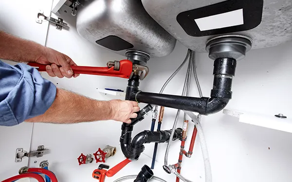 Skilled plumber using wrench to repair drainpipe under kitchen sink during local residential plumbing service in Sunnyvale TX.
