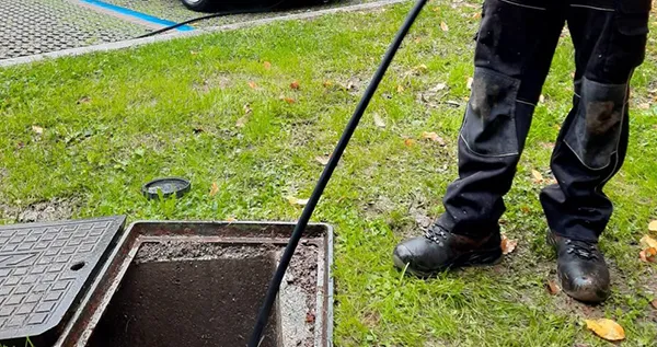 Worker performing drain pipe inspection using a tool near an open outdoor drain in Travis Ranch TX.