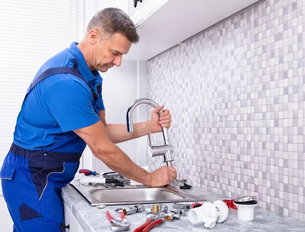 Professional plumber fixing pipe under kitchen sink with wrench in Terrell TX residence, offering 24/7 emergency plumbing.