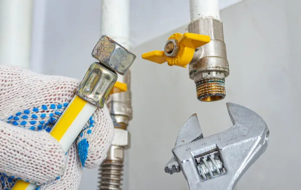 Plumber’s hand using an adjustable wrench to tighten a gas line connection on a flexible braided hose.