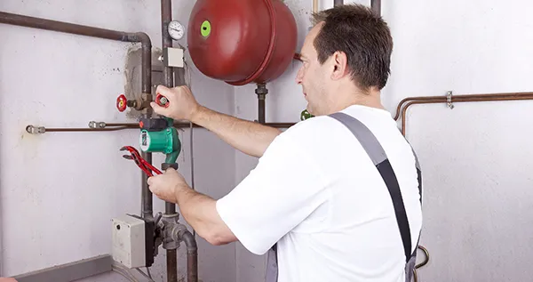 Technician wearing white shirt using power tool to work on gas line equipment in a basement.