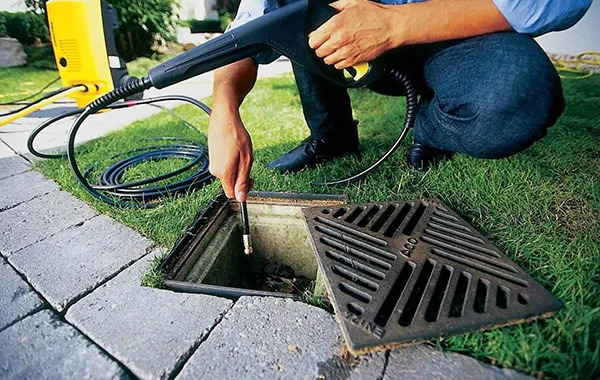 Technician using drain cleaning equipment to unclog outdoor storm drain grate in Garland TX residential area.