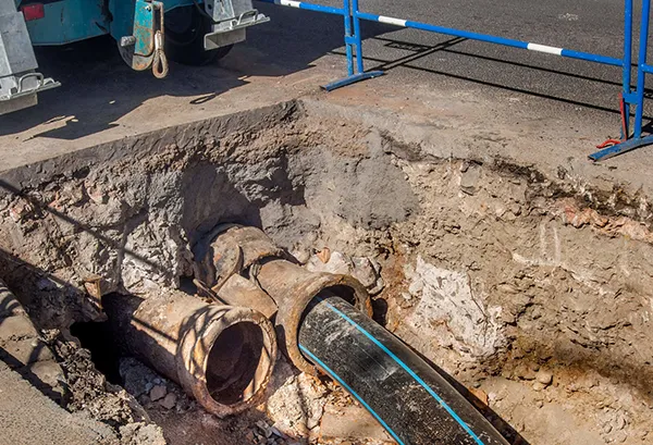 Excavation site showing old sewer pipes and plumbing repair equipment in a trench.