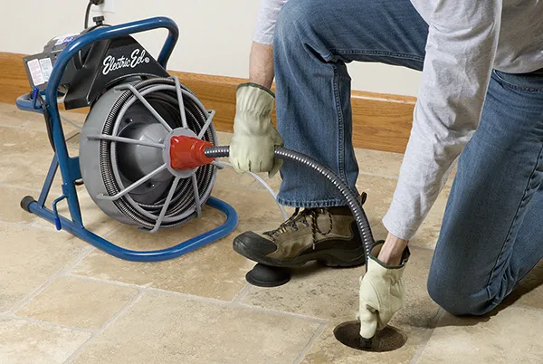 Professional plumber using a drain cleaning machine to clear a clogged pipe.
